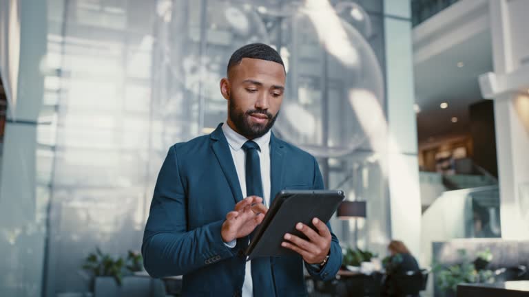 Businessman working on a digital tablet while walking in a corporate office. Marketing professional and black man doing research on the internet or a website with a mobile device for startup project